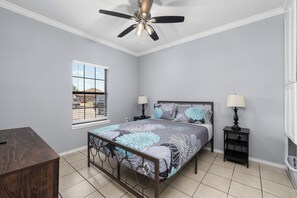 A bedroom with a bed, two bedside tables, a ceiling fan, a window with blinds, and a view of the outside. - The C2 Gateway to Starbase (Brownsville)