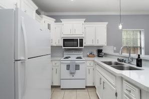 A modern kitchen with white cabinetry, a stainless steel sink, and a built-in microwave. - The C2 Gateway to Starbase (Brownsville)