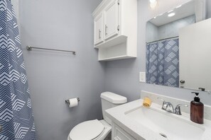 A bathroom with a white toilet, a sink with a soap dispenser, and a shower curtain with a geometric pattern. - The C2 Gateway to Starbase (Brownsville)