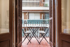 Blick durch eine Holztür auf einen Balkon mit Tisch und Stühlen, gefliester Boden und eine Backsteinwand.