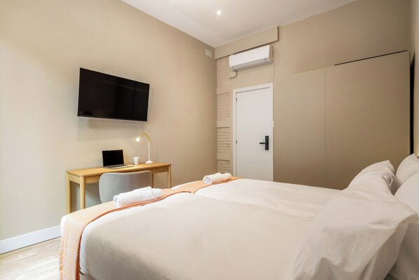 Ein Hotelzimmer mit Bett, Schreibtisch mit Laptop, Wand-Fernseher und einer Tür.