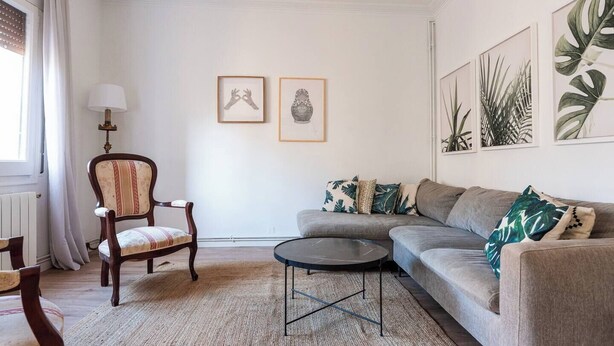 Ein Wohnzimmer mit Sofa, Sessel und Couchtisch, einem Heizkörper und gerahmten Kunstwerken an der Wand.