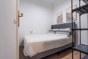 A single bed with a grey headboard, white bedding, and striped pillows. There is a power outlet on the wall, and two abstract art pieces are hung above the bed. - Modern, spacious monthly rental (min 32 nights) in the city centre (Barcelona)