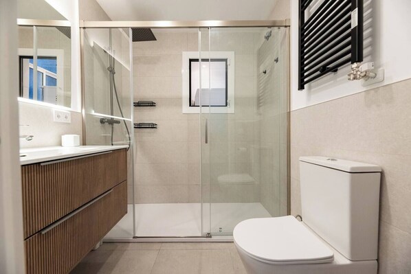 A modern bathroom with a glass-enclosed shower, a wooden vanity, and a white toilet. - Modern, spacious monthly rental (min 32 nights) in the city centre (Barcelona)