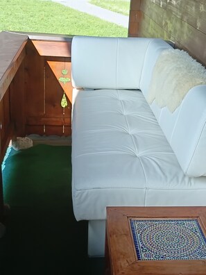Ein weißes Ledersofa mit einer flauschigen weißen Decke, eine Holzbank mit einer dekorativen Aussparung und ein mit geometrischen Mustern versehener Couchtisch mit Fliesen.