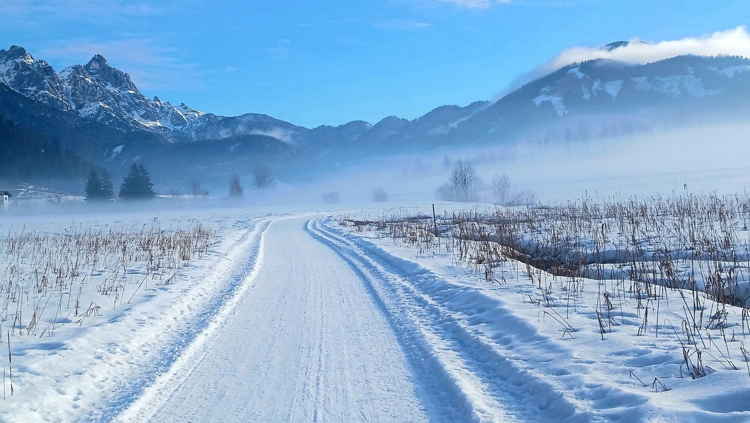 Eine verschneite Straße mit Bergkulisse.