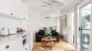 Eine moderne Küche mit weißen Schränken, ein Essbereich mit rundem Tisch und ein Wohnzimmer mit dunkelgrauem Sofa und grünen Kissen.