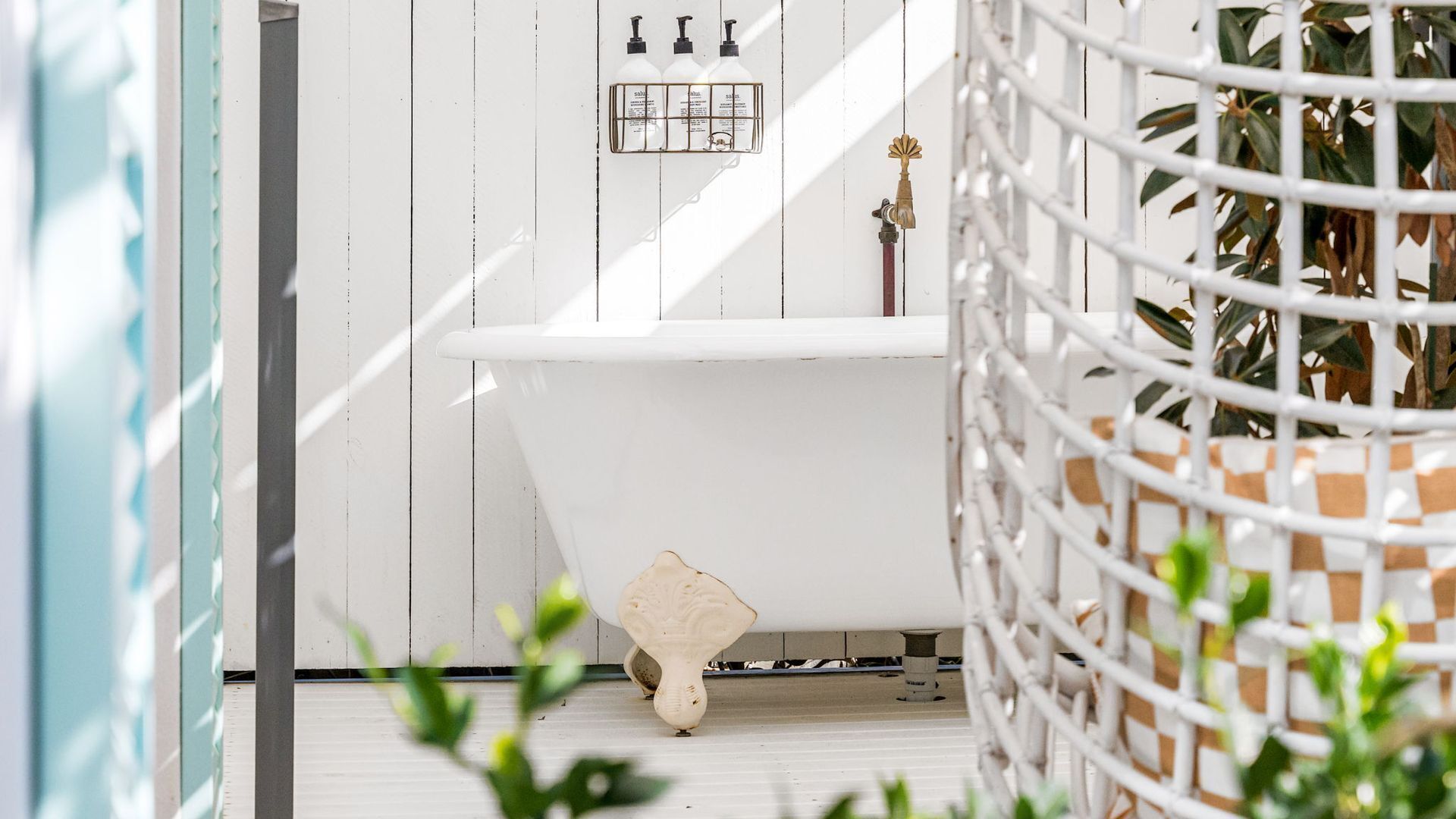 A white bathtub with a showerhead, a small stool, and a wall-mounted soap dispenser.