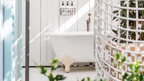 Una bañera blanca con cabezal de ducha, un taburete pequeño y un dispensador de jabón en la pared.