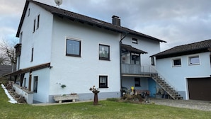 Un edificio de dos pisos con antena parabólica, un balcón y una escalera que da a un garaje.