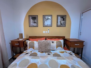 Ein Schlafzimmer mit einem Bett, zwei Nachttischen, einem Beistelltisch und drei gerahmten Bildern an der Wand.