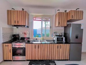 A modern kitchen with wooden cabinets, a stainless steel refrigerator, an oven, and a microwave. - Cité Italia - Quiet & elegant villa with garden/terrace - near the beaches (Modest)