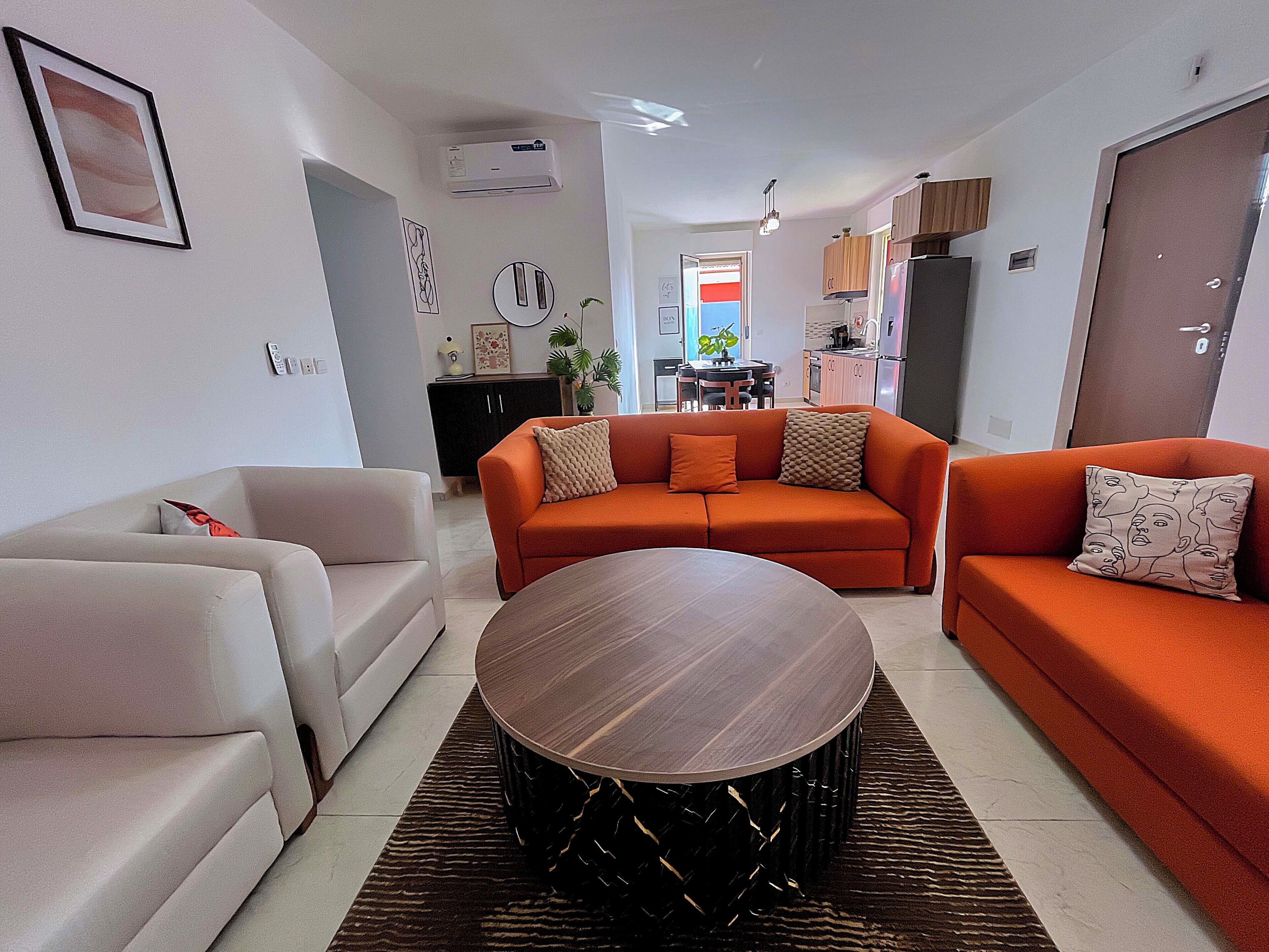 A modern living room with a sofa, a dining table, and a kitchen in the background.