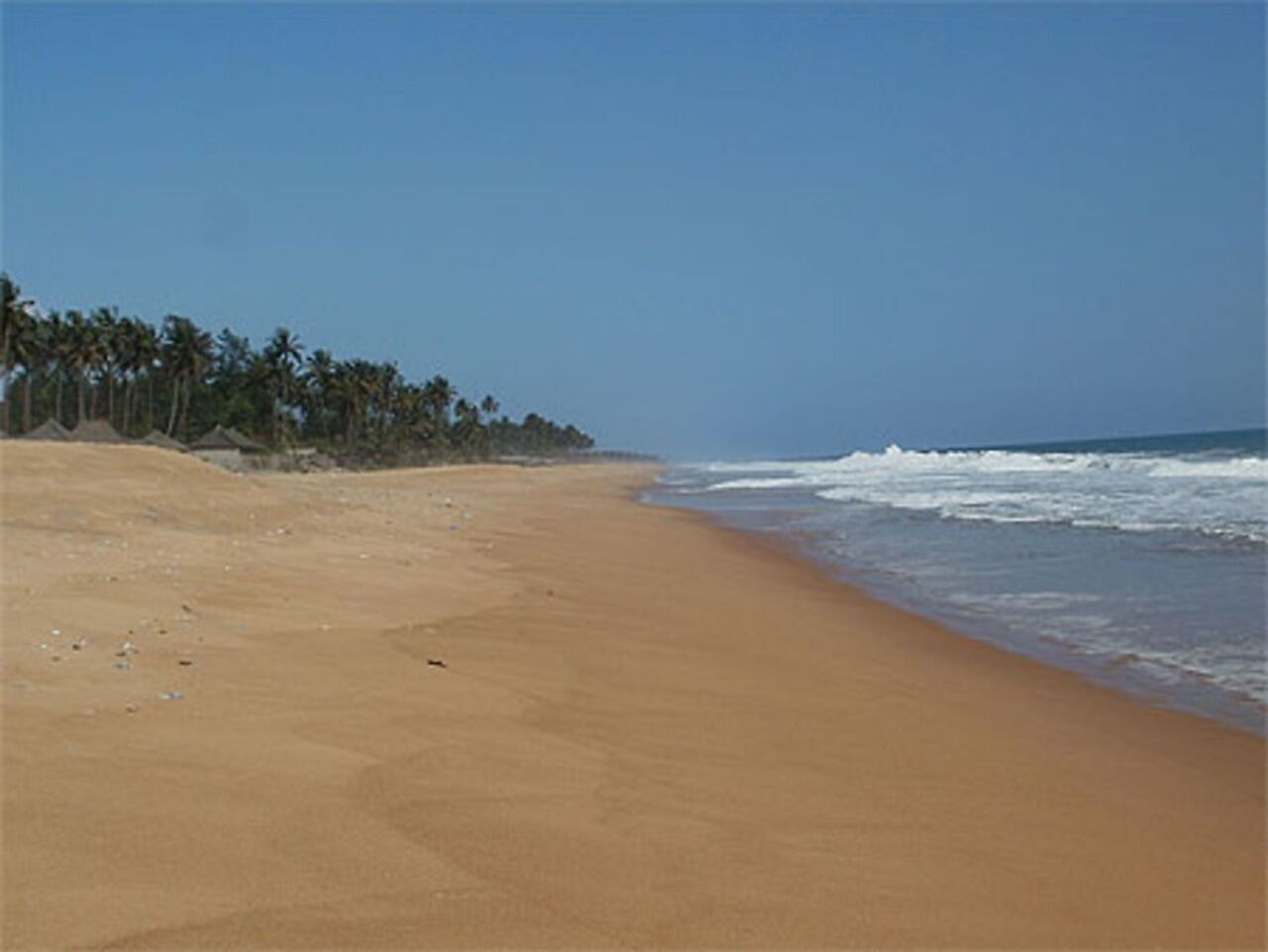 Une plage de sable fin, avec un ciel dégagé et des vagues sur l’océan.