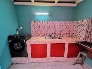 A compact kitchen with a washing machine, a sink, and a tiled backsplash.