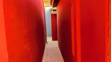 Un couloir étroit aux murs rouges et au sol en briques, qui mène à une porte au fond.