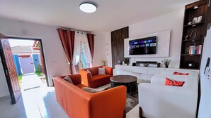 A modern living room with a sofa, armchairs, a coffee table, a flat-screen TV, and a bookshelf. - Cité Italia - Quiet & elegant villa with garden/terrace - near the beaches (Modest)