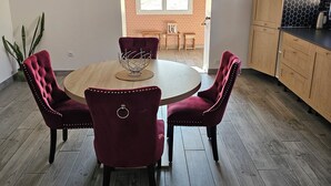 A dining area with a round table and four chairs, a kitchen with wooden cabinets, and a view through a window to an outdoor area. - Under the stars in the countryside (Paray-le-Frésil)