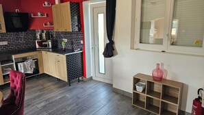 A compact kitchen with a microwave, oven, and wooden cabinets. There is a dining area with a red chair and a small wooden shelf. - Under the stars in the countryside (Paray-le-Frésil)