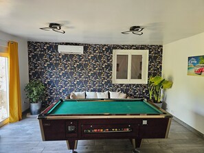 A pool table in a room with patterned wallpaper, a window, and a potted plant. - Under the stars in the countryside (Paray-le-Frésil)