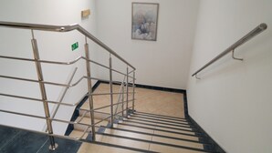 Een trap met metalen leuningen, een groen nooduitgangsbord en een lijst met bloemkunst aan de muur.