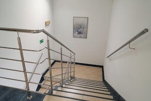 Una escalera con barandillas de metal, un letrero de salida de emergencia verde y una obra de arte floral enmarcada en la pared.