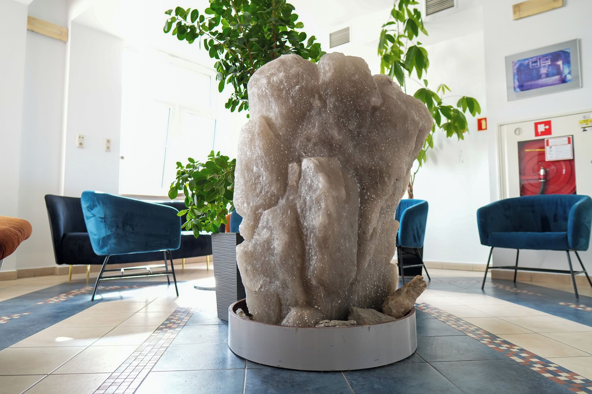 Ett entrérum med en central skulptur i form av en klippa, blå stolar och en krukväxt.