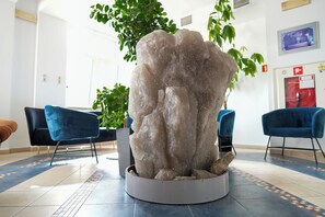 A reception area with a central rock sculpture, blue chairs, and a potted plant.