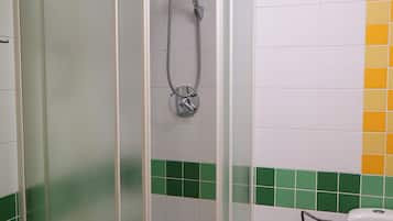 Compartimento de chuveiro com porta de vidro, chuveiro manual e vaso sanitário com função bidê.