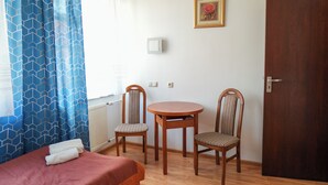 Een kamer met een bed, twee stoelen, een tafeltje, een deur en een lichtschakelaar aan de muur.