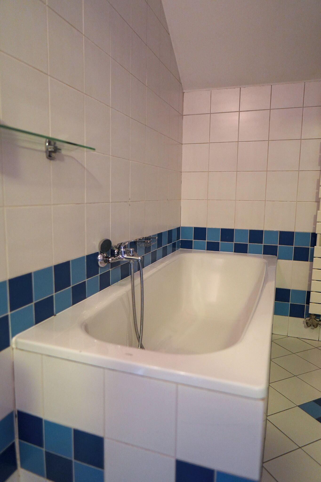 Un baño con una bañera blanca, paredes con azulejos azules y un estante de vidrio.