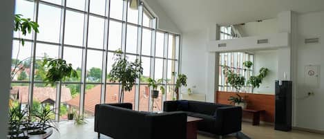 A spacious lobby with large windows, black sofas, and multiple potted plants.