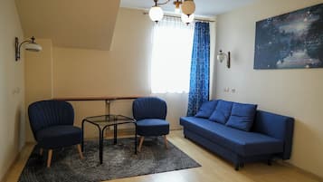 Uma sala de estar moderna com um sofá azul, duas poltronas, uma mesa de centro de vidro, um lustre e um quadro na parede.