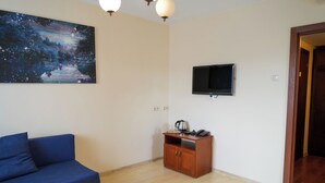 A room with a blue sofa, a wooden cabinet with a kettle, glasses, and a phone, a flat-screen TV mounted on the wall, and a painting of a night sky. - Hotel Sutoris (Bochnia)