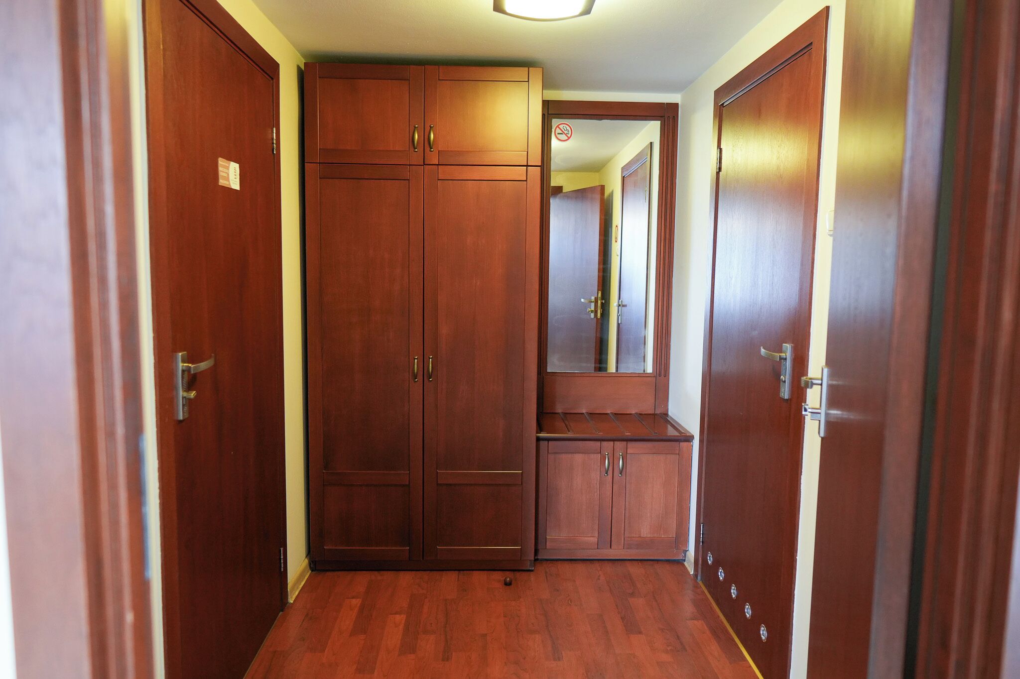 A hallway with wooden wardrobes, a mirror, and a door with a no-smoking sign.