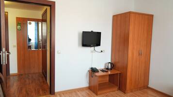 Una habitación con un armario de madera, un escritorio pequeño con teléfono y hervidor, y un televisor fijado a la pared.