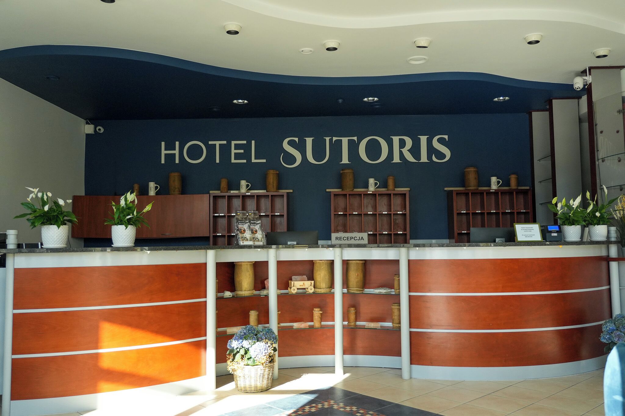 Ein Empfangstisch mit einem Schild, auf dem 'HOTEL SUTORIS' und darunter 'RECEPCJA' steht.