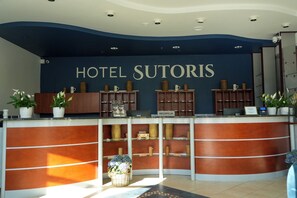 A reception desk with a sign reading 'HOTEL SUTORIS' and a 'RECEPCJA' sign below it.
