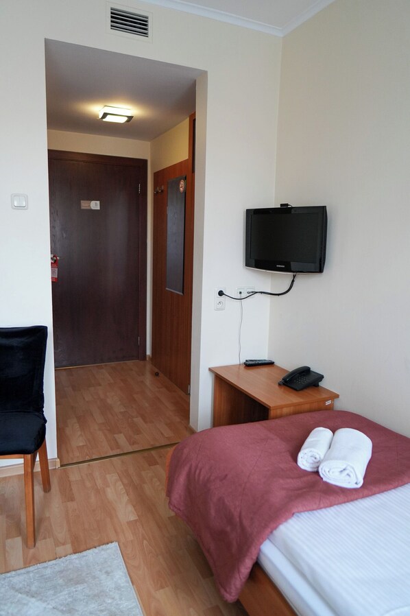 Habitación de hotel con cama, escritorio con teléfono, televisor montado en la pared, una silla y una puerta.