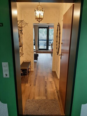 A hallway with a wooden floor, a bench, a table, a chandelier, and a view through a glass door. - Mozartschwänchen, 60 square meters (Bad Reichenhall)