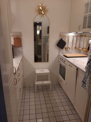 A compact kitchen with white cabinets, a marble countertop, a small stool, and a hanging utensil rack. - Mozartschwänchen, 60 square meters (Bad Reichenhall)
