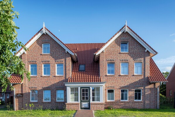 Ein zweistöckiges Backsteinhaus mit Ziegeldach, einem zentralen Eingang mit Glastür und zahlreichen Fenstern.