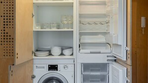Una cucina compatta con lavatrice integrata, scaffali per stoviglie e frigorifero.