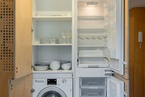 Eine kleine Küche mit integriertem Waschmaschinen, Geschirrregalen und einem Kühlschrank.