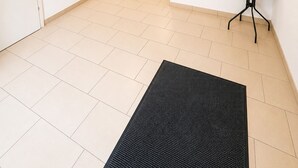 Ein Flur mit einer schwarzen Matte, einem kleinen Tisch mit einer Pflanze und einem Feuerlöscher.