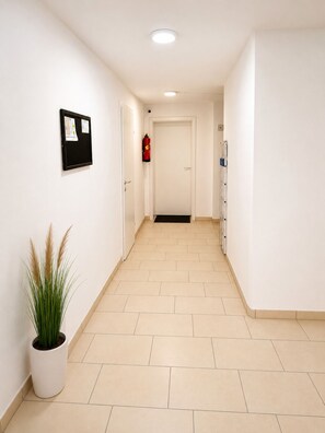 A clean, well-lit hallway with a fire extinguisher mounted on the wall, a bulletin board, and a potted plant. - MODERN HOLIDAY APARTMENT Free
Parking Free WiFi Fully Equipped 1 to 4
Guests (Wolkersdorf)