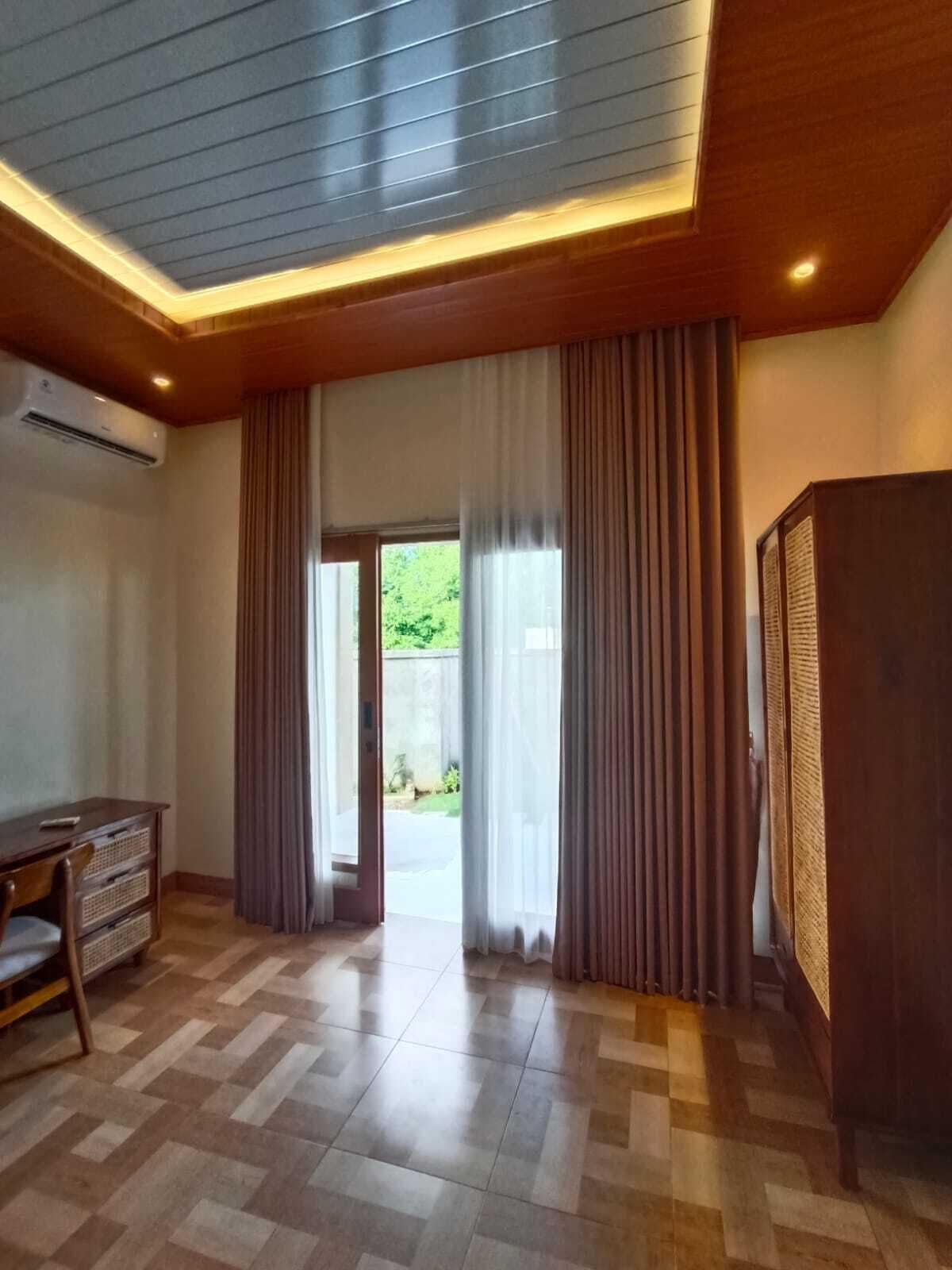 Une pièce avec un plafond en bois, une grande fenêtre avec des rideaux, un téléviseur à écran plat et un sol carrelé.
