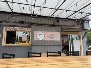 A restaurant with a sign reading "BANANA WINDOW" and another sign indicating "Now Open!!" with a list of menu items. - Oceanfront Retreat with Panoramic Views & Beachfront Lanai -Mahana (Lahaina)