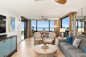 A spacious living area with a view of the ocean, a dining set, and a television. - Oceanfront Retreat with Panoramic Views & Beachfront Lanai -Mahana 109 (Lahaina)