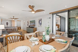 A modern dining area with a wooden table set for a meal, surrounded by wicker chairs. - Oceanfront Retreat with Panoramic Views & Beachfront Lanai -Mahana 109 (Lahaina)